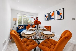 A modern dining area with a glass table, orange upholstered chairs, and abstract art on the wall. - Stylish Catford Maisonette + Free Parking (London)