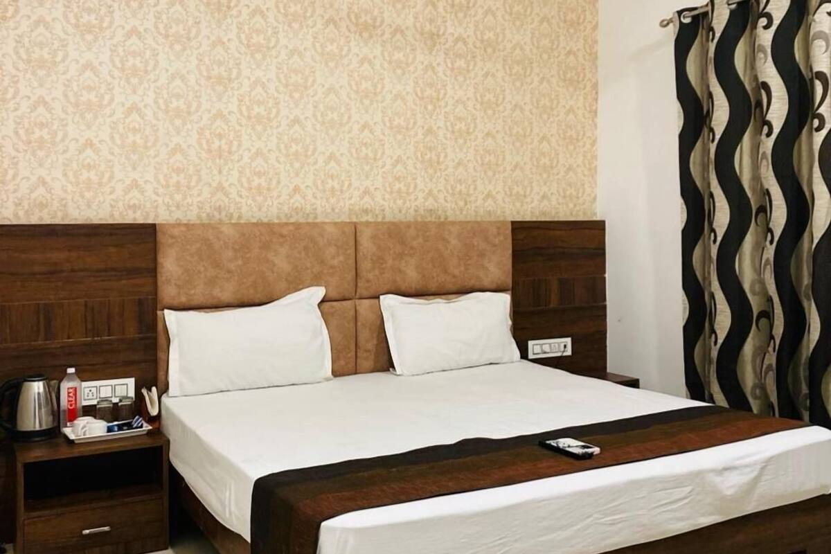 Habitación de hotel con cama, cabecero de madera, mesitas de noche, ventilador de techo, papel tapiz estampado y cortina.