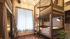 Ein Schlafzimmer mit Etagenbetten, einer Leiter, Holzboden und einem Fenster mit Vorhängen.