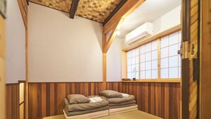 Ein traditioneller japanischer Raum mit Tatami-Böden, einem niedrigen Holzbett, einem Shoji-Bildschirm und einer Decke mit freiliegenden Balken.