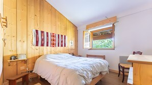 Quarto com painéis de madeira, uma cama, uma escrivaninha e uma janela.