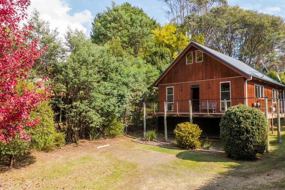 Una casa de madera rústica con un porche cubierto, rodeada de árboles frondosos y un césped cuidado.