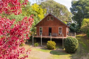 Una cabaña de madera con terraza, rodeada de árboles y un césped cuidado.