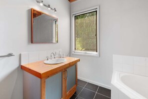 Un baño con tocador de madera, un lavabo blanco, un espejo, una ventana con persianas y una bañera blanca.