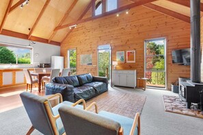 Ein geräumiger Wohnbereich mit Holzvertäfelung, einer Couch, Sesseln, einem Kamin und einem Fernseher.