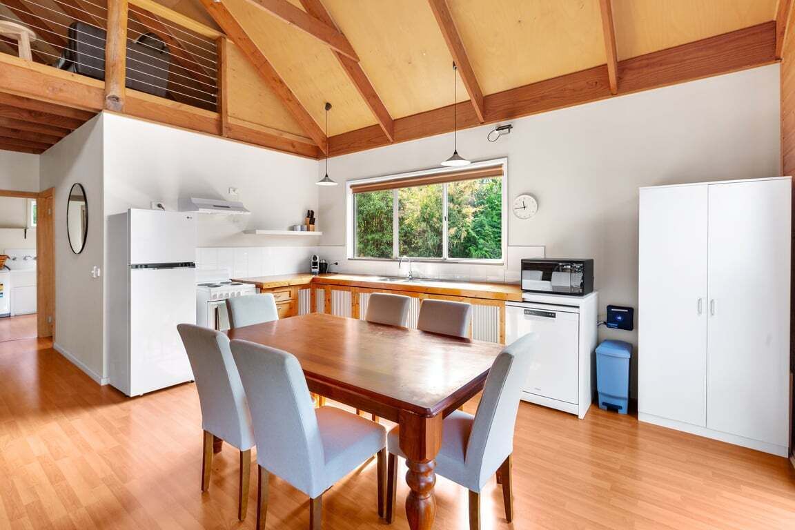 Een moderne keuken met witte kastjes, een houten eettafel met stoelen en een groot raam voor natuurlijk licht.
