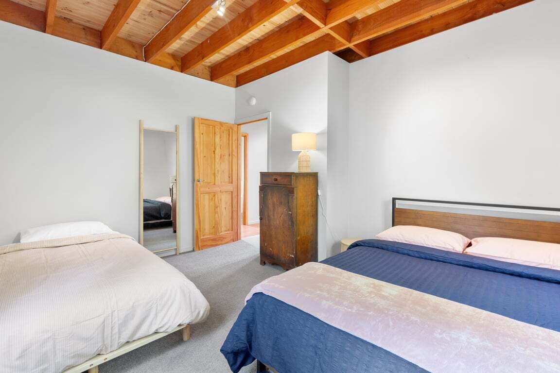 Slaapkamer met twee bedden, houten balken in het plafond, een houten garderobe en een spiegel.