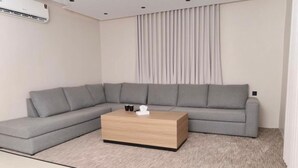 A modern living room with a grey sectional sofa, a wooden coffee table, and a large window with curtains. - Moodar (Madinah)