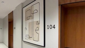 A hallway with a framed abstract artwork, a wooden door, and a number '104' on the wall. - Moodar (Madinah)