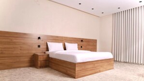 A modern bedroom with a wooden headboard, a single bed, a nightstand, and a large window with vertical blinds. - Moodar (Madinah)