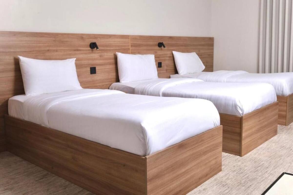 A hotel room with three wooden beds, each with white bedding and headboards.