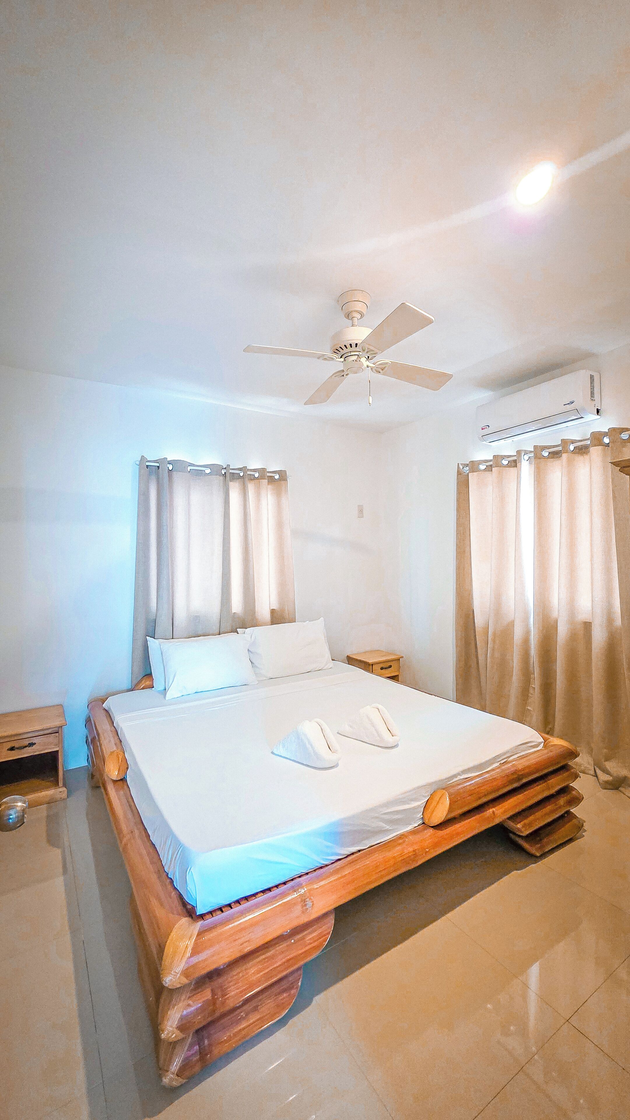 A bedroom with a bed, a ceiling fan, curtains, and a wall-mounted air conditioning unit.