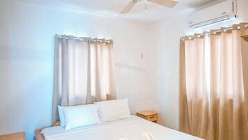 A bedroom with a bed, a ceiling fan, curtains, and a wall-mounted air conditioning unit.