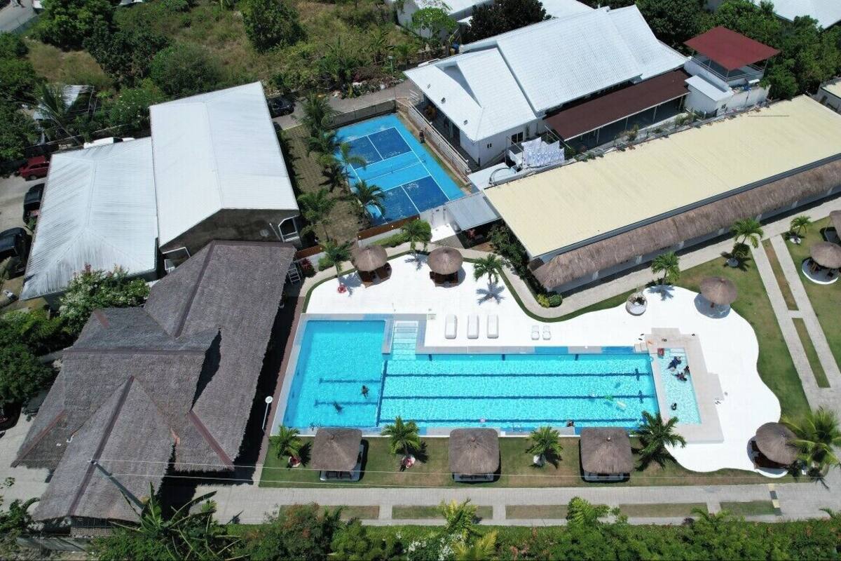 An aerial view of a resort with a large swimming pool, multiple buildings, and thatched-roof structures.