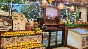 A restaurant interior with a tropical theme, featuring hanging fruit, a floral tablecloth, and a bar area.