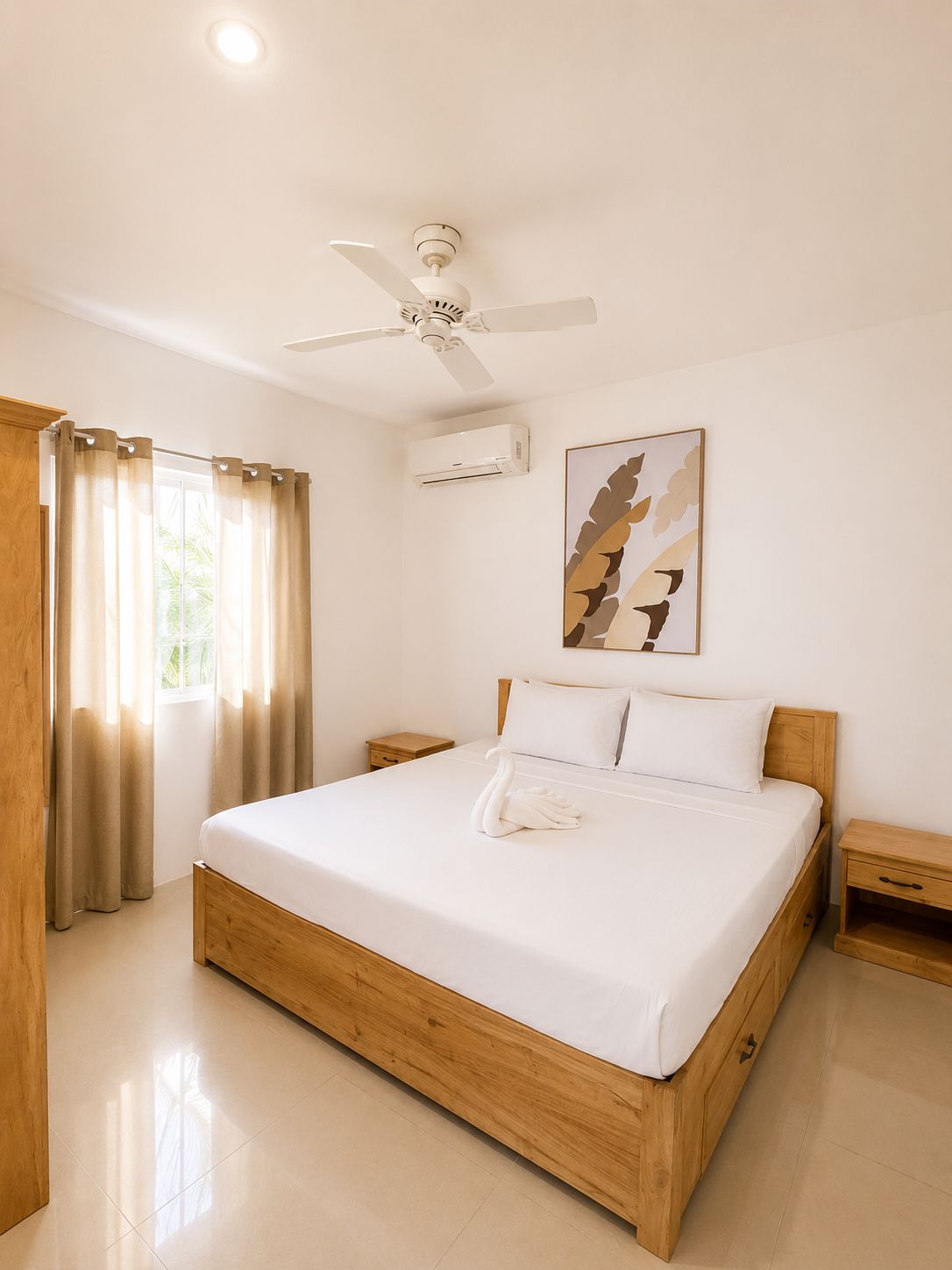 Habitación de hotel con cama de madera, ventilador de techo, unidad de aire acondicionado, ventana con cortinas y una obra de arte colgada en la pared.