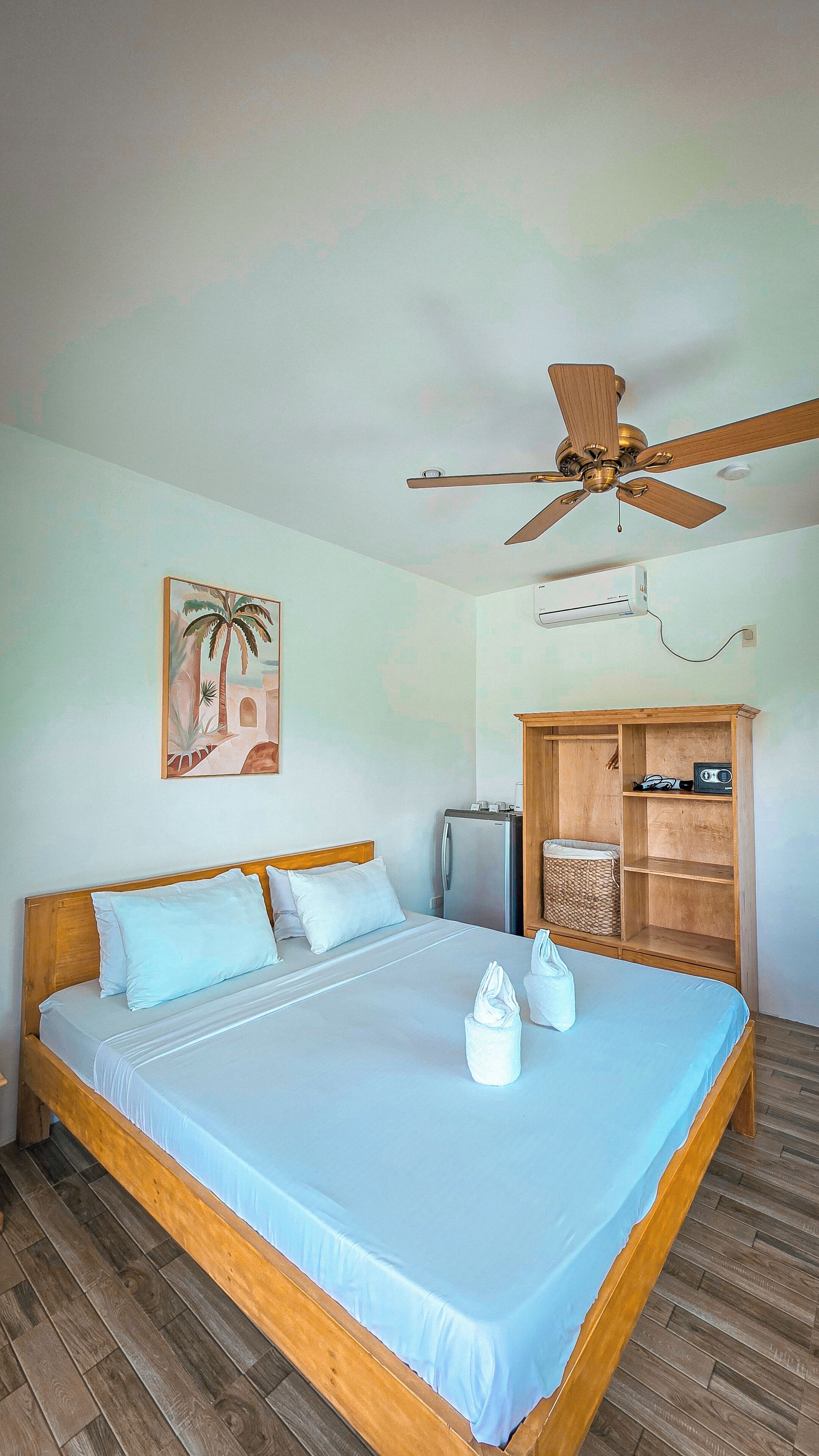 A bedroom with a bed, a ceiling fan, a wall-mounted air conditioner, a television, and a wooden cabinet.