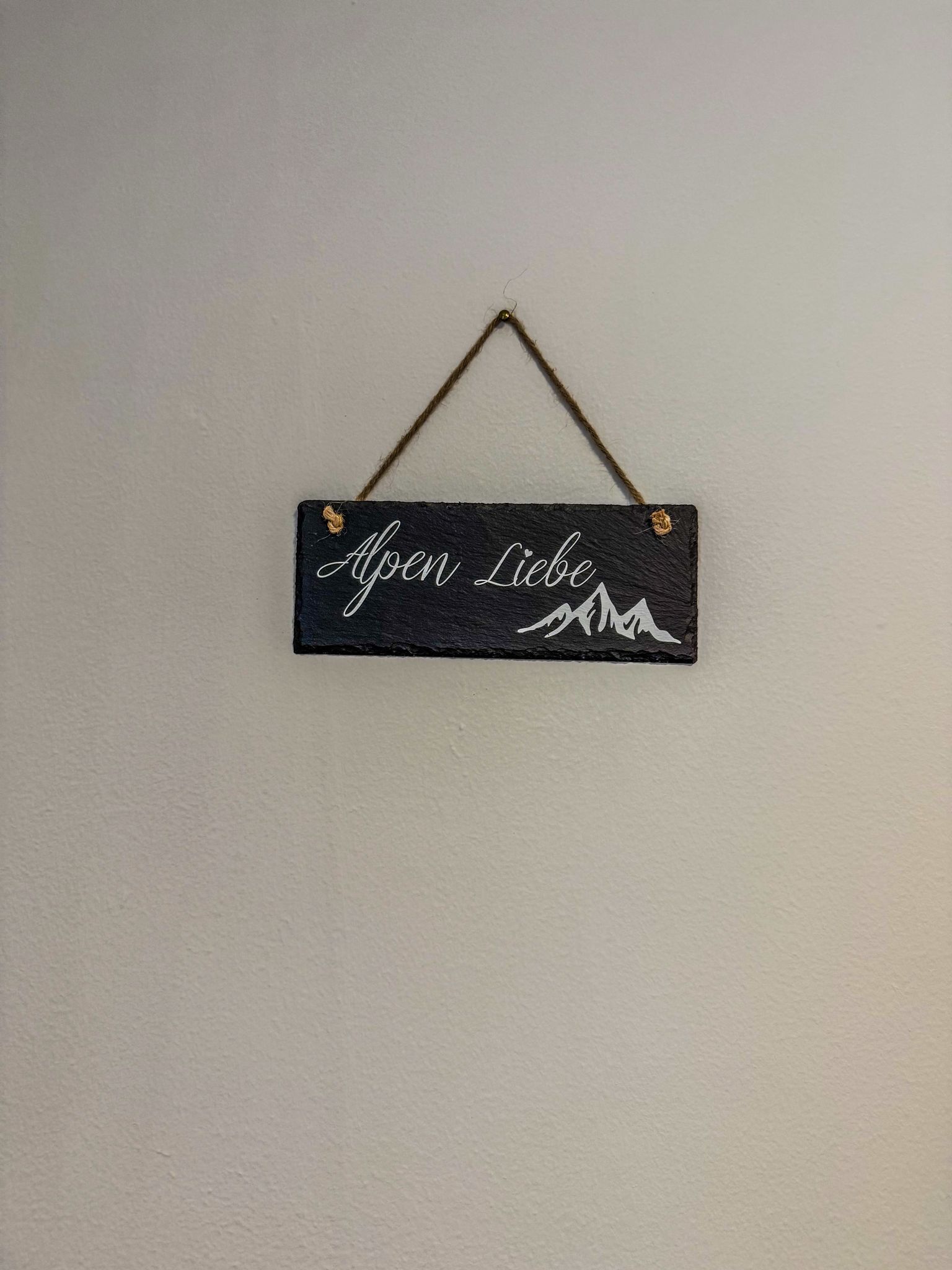 Et sort skilt med hvid tekst og en bjergillustration, hængende på en ensfarvet væg.