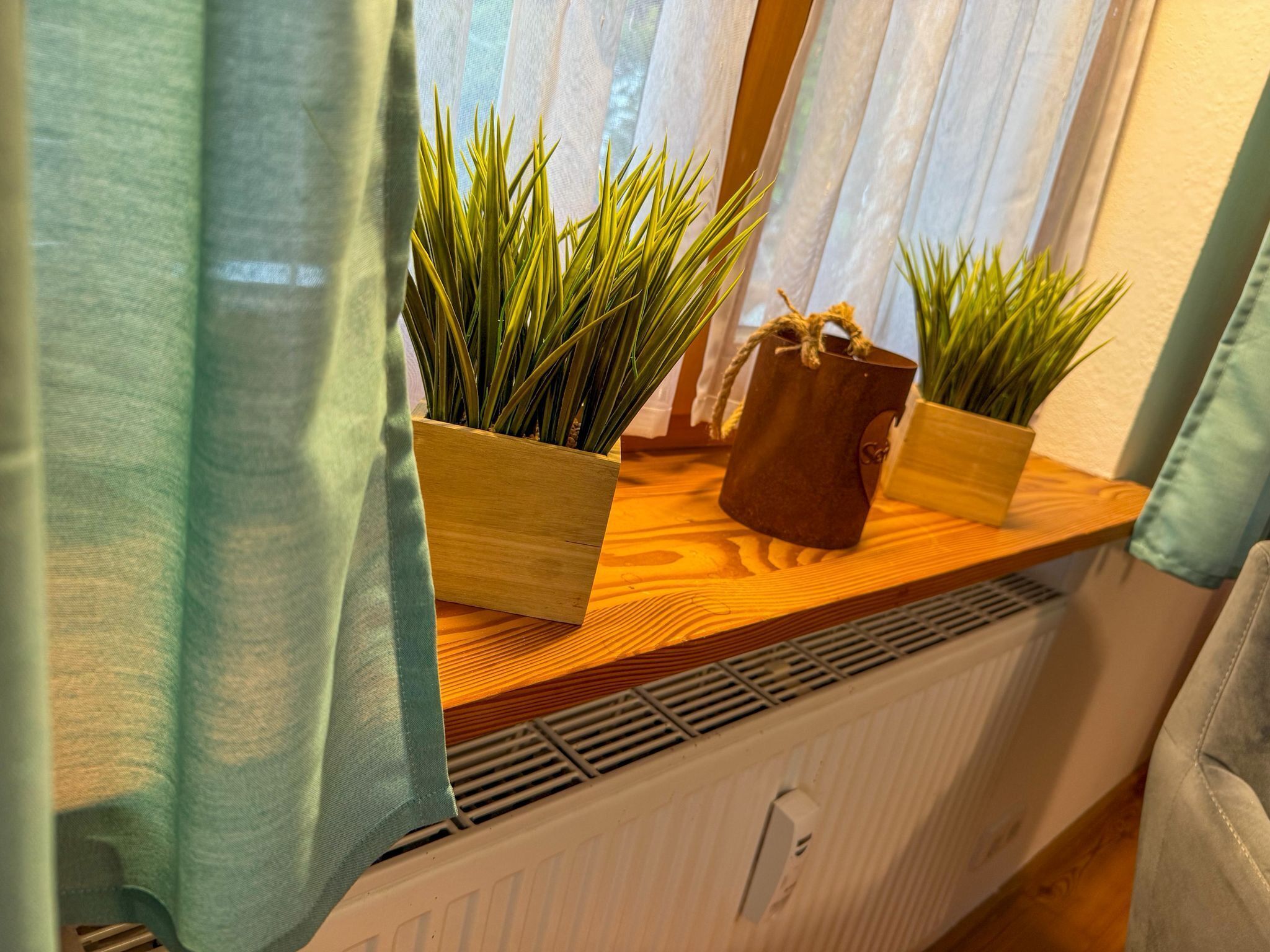 A window with curtains, two wooden planters with green plants, and a radiator below.