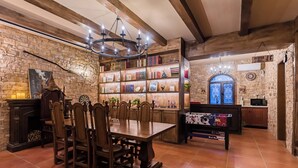 A dining area with a wooden table and chairs, a chandelier, a bookshelf with books and decorative items, and a stone wall. - Beijing Magic Villa (Tongzhou)