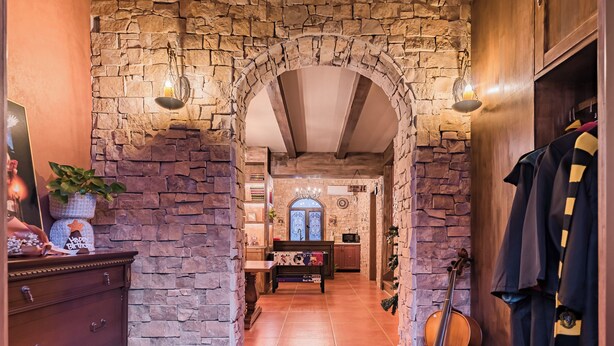 A stone-walled hallway with a violin, a wooden cabinet, and a bench with a patterned cushion. - Beijing Magic Villa (Tongzhou)