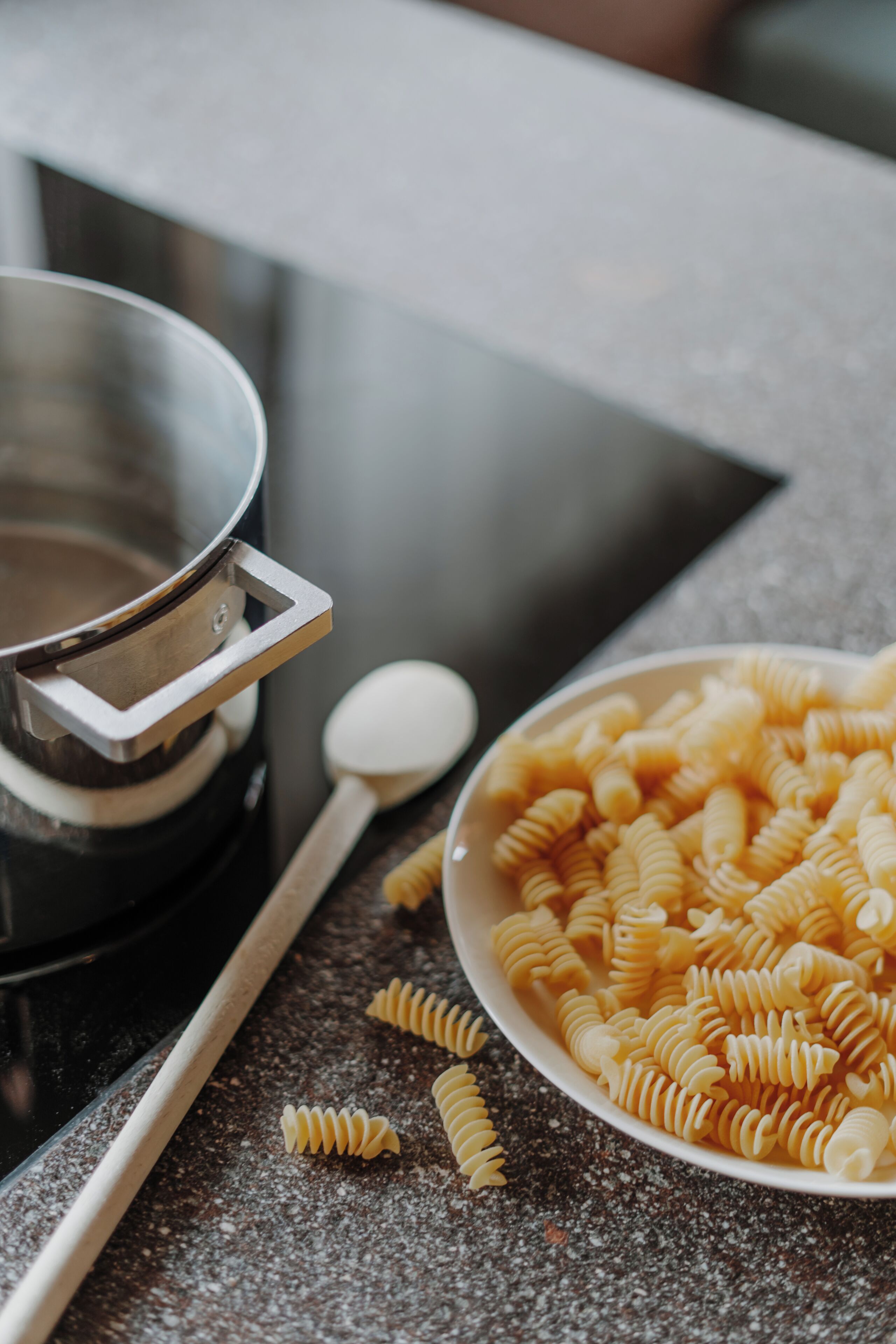 Un plan de travail de cuisine avec une casserole, un bol de pâtes et une cuillère.