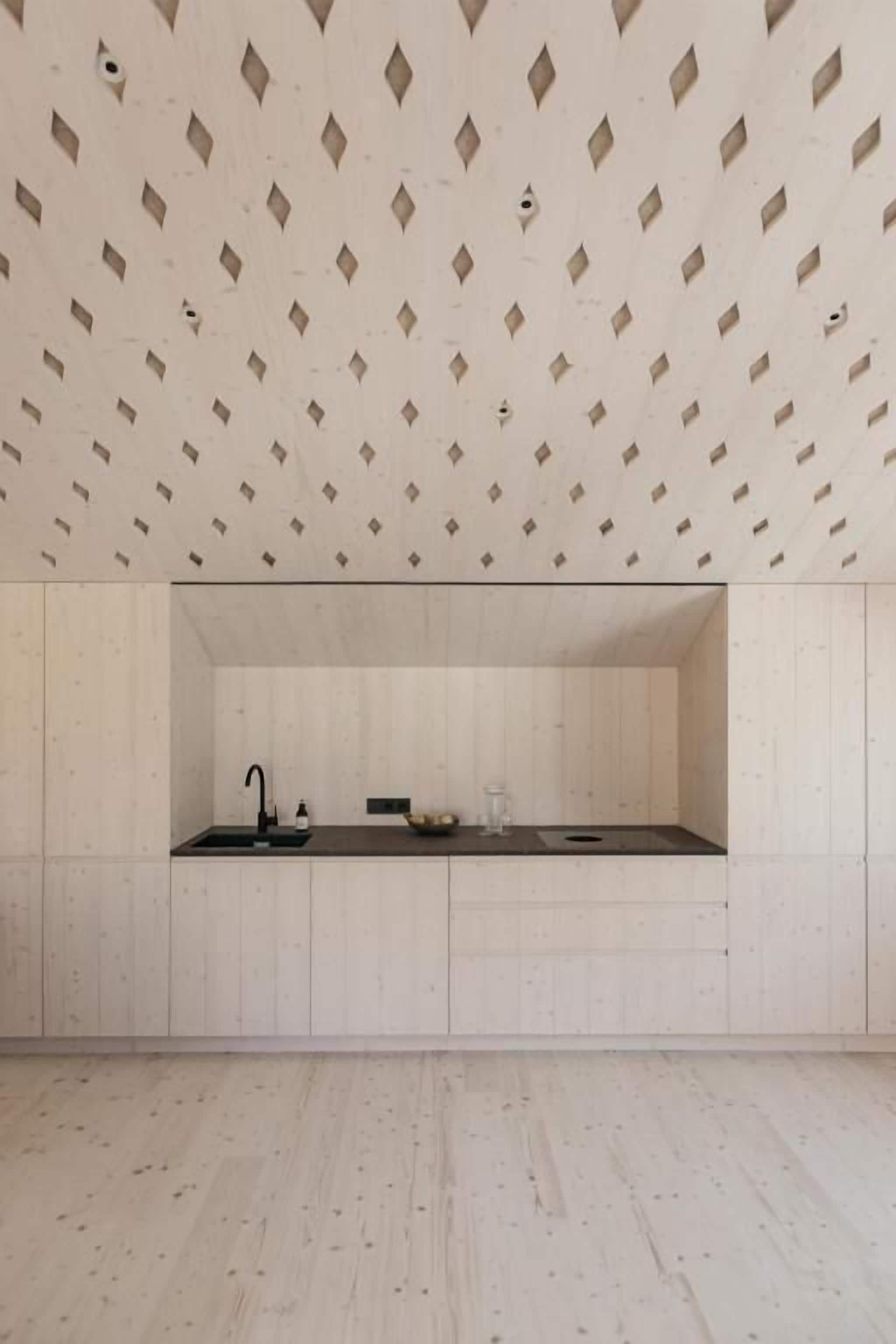 Una cocina minimalista con un patrón geométrico en el techo, un grifo negro y una encimera sencilla.