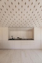 Una cocina minimalista con un patrón geométrico en el techo, un grifo negro y una encimera sencilla.