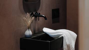 Un baño con un lavamanos negro, un espejo, un florero con flores secas y una toalla.