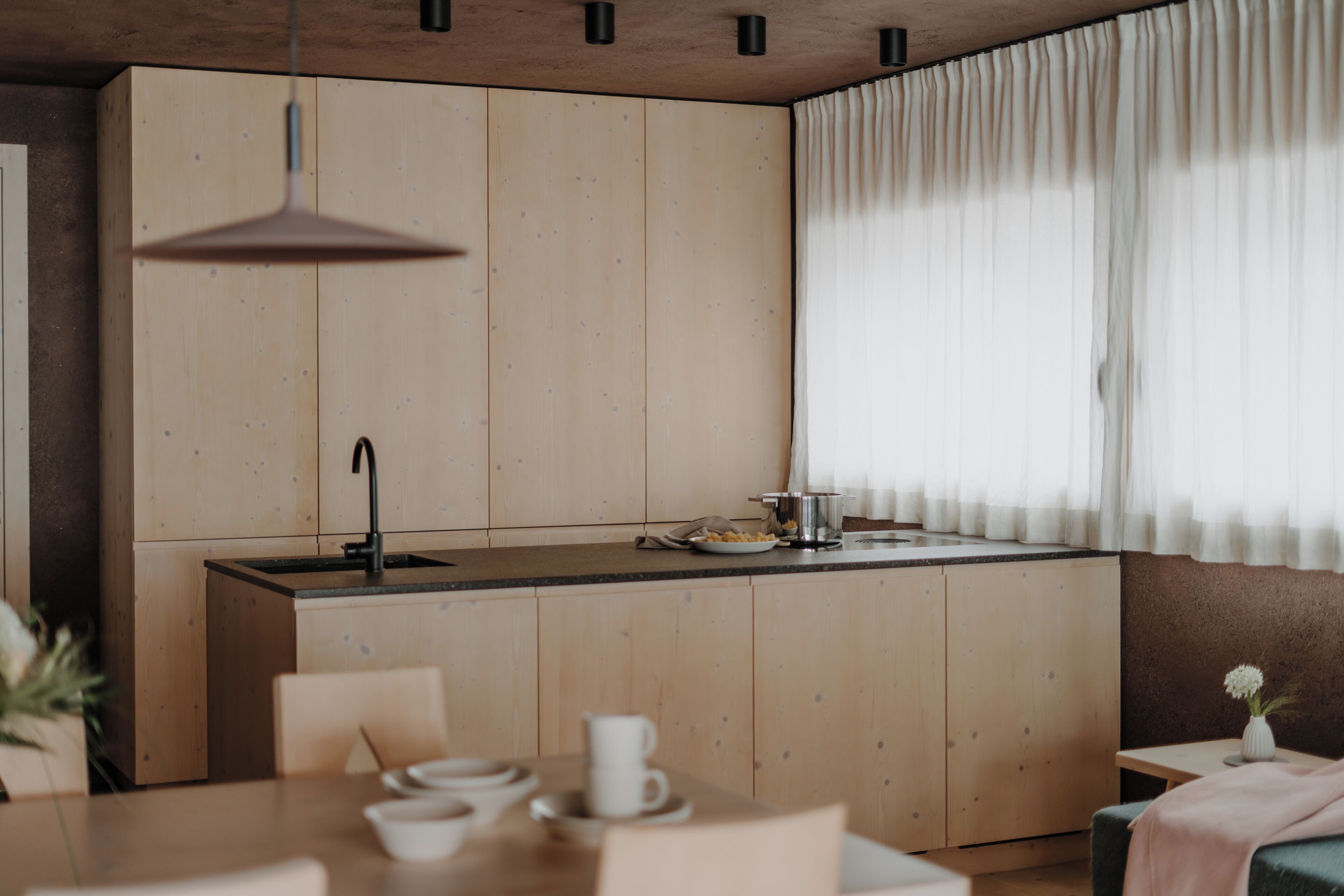 A modern kitchen with wooden cabinets, a central island, a sink, and a dining area with chairs and a table.