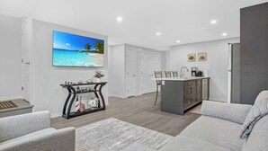 Ein modernes Wohnzimmer mit grauem Sofa, Couchtisch und Fernseher, der eine Strandansicht zeigt.