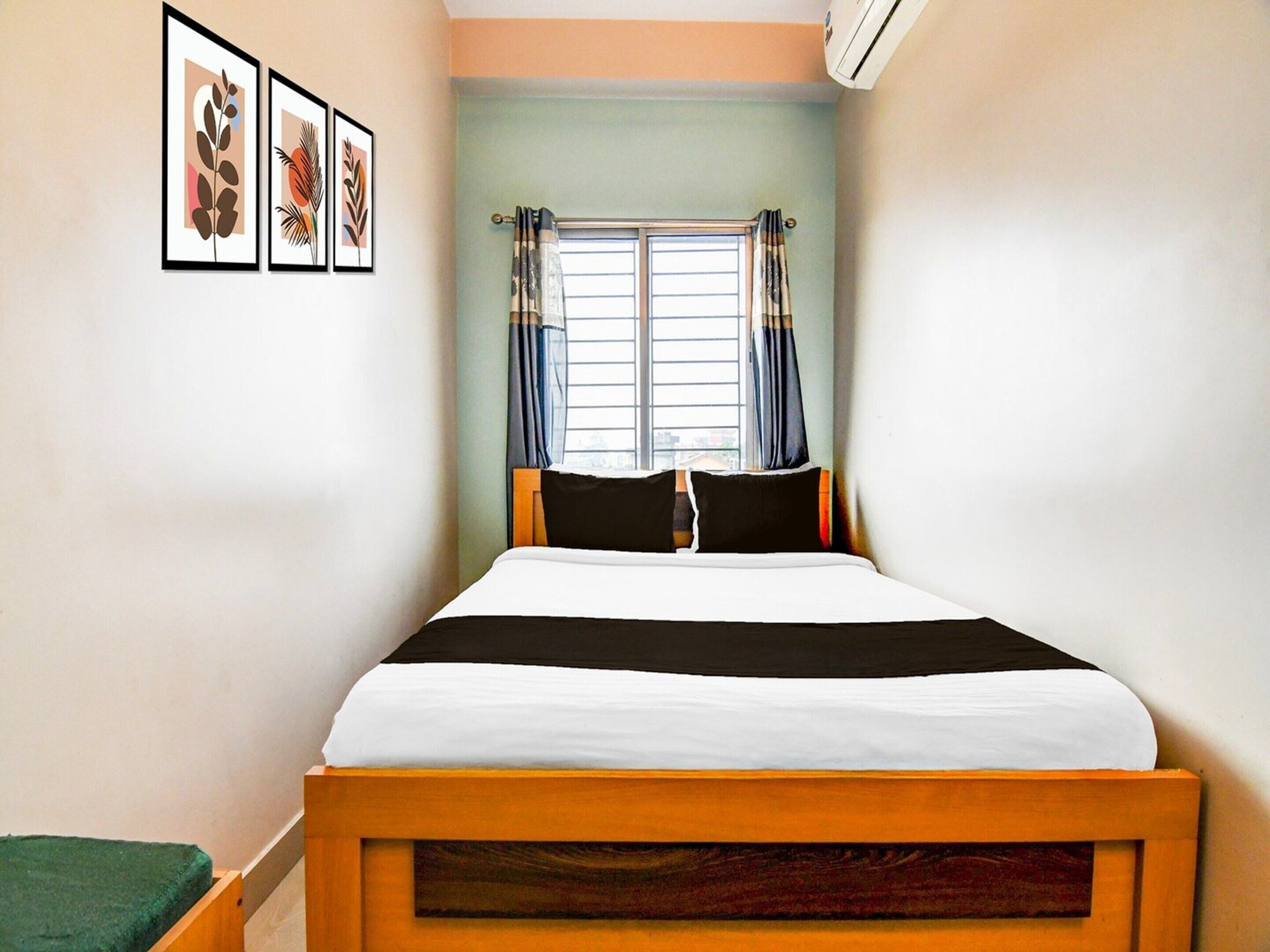 Een kamer met een bed, een raam met gordijnen en kunstwerken in een lijst aan de muur.