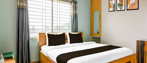 A hotel room with a bed, a window with curtains, a bedside table, a mirror, and wall art.