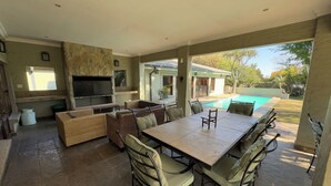 Eine Terrass mit Essbereich, Stühlen, einem Fernseher und einem Pool.