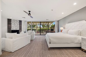 A hotel room with a bed, two white armchairs, a ceiling fan, and a view through a glass door. - Courtside Escape - Country Club Living (Rancho Mirage)