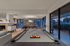 A pool table with balls, a sofa, a fireplace, and a dining area with chairs and a table. - Courtside Escape - Country Club Living (Rancho Mirage)