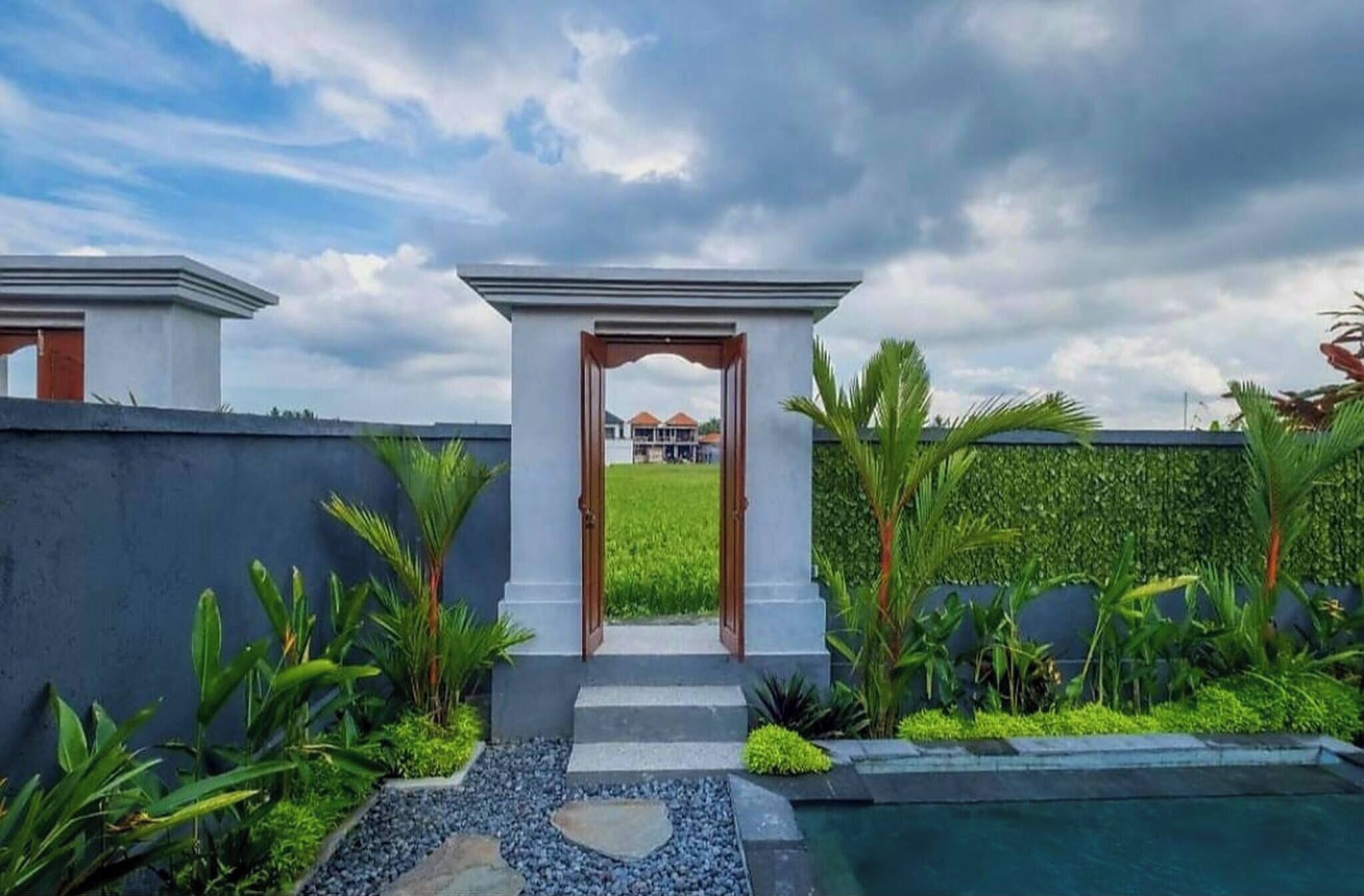 A modern architectural structure with a central archway leading to a lush garden and a pool.