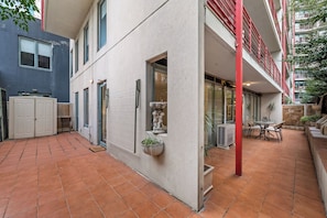 A courtyard with a tiled floor, a seating area with a table and chairs, and a building with a red railing and multiple windows. - Exclusive Stays - Southbank Towers (Southbank)