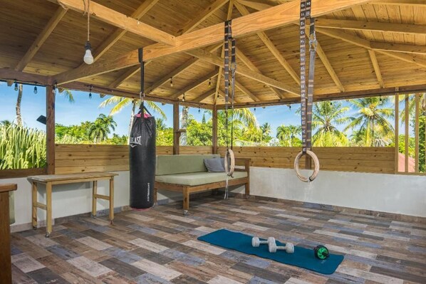 An open-air gym with wooden flooring, exercise equipment, a punching bag, and a bench.