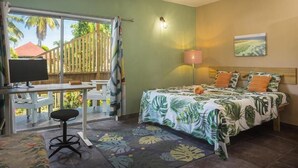 Ein Zimmer mit Bett, Schreibtisch, Stuhl, Fernseher und Blick auf Palmen.