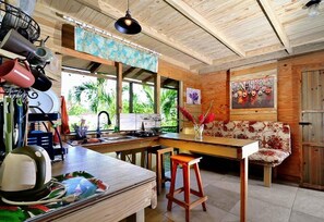 A kitchen with a wooden ceiling, a dining area with a table and chairs, and a view of greenery outside.