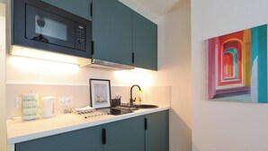 Eine moderne Küche mit türkisfarbenen Schränken, einer Mikrowelle, einem Wasserkocher und einem Bild an der Wand.