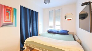 Ein Schlafzimmer mit einem Bett, einem Fenster mit Jalousien, einem Spiegel und einem Bild an der Wand.