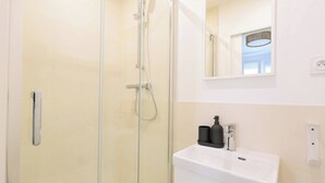 Ein modernes Badezimmer mit Duschkabine aus Glas, einem weißen Waschbecken und einem Spiegel darüber.
