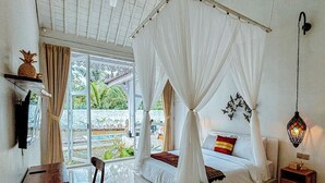 A room with a bed, a chair, a small table, a nightstand, a hanging light, and a window with curtains. - Hafrana Villa by AGATA - 700sqm 2BR Villa with Private Pool & Jacuzzi (Selat)