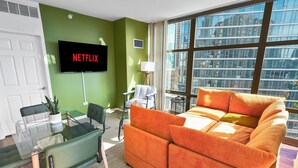 A modern living room with a green wall, a large window, a sofa, a TV, and a glass table. - Skyline 2BR Heart of Chicago Walk to Grant Park (Chicago)