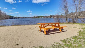 Ein Picknicktisch an einem sandigen Strand mit einem See und Bäumen im Hintergrund.