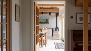 A narrow hallway leading to a dining area with a wooden table and chairs, a kitchen with a view of a landscape, and a staircase on the right. - Blackhill barn - in the heart of the Cotswolds (Craswall)