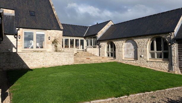 A stone building with a grassy courtyard, large windows, and a staircase leading to the entrance. - Blackhill barn - in the heart of the Cotswolds (Craswall)