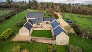 A large, stone farmhouse with multiple attached buildings, surrounded by lush green fields and a forested area. - Blackhill barn - in the heart of the Cotswolds (Craswall)